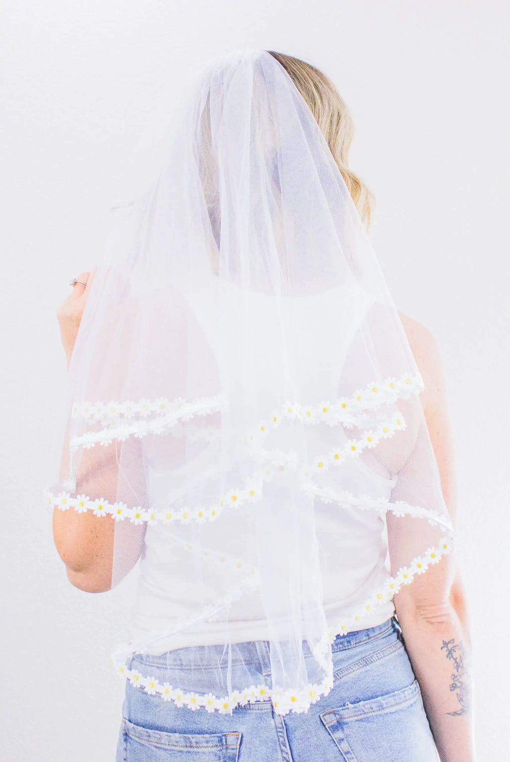 Person wearing a white veil with floral trim on a plain background