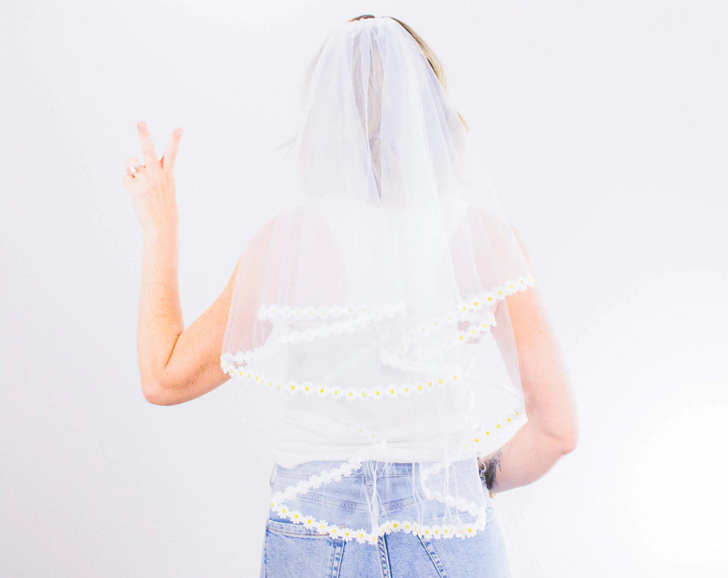 Person wearing a white lace veil and denim skirt on a light gray background